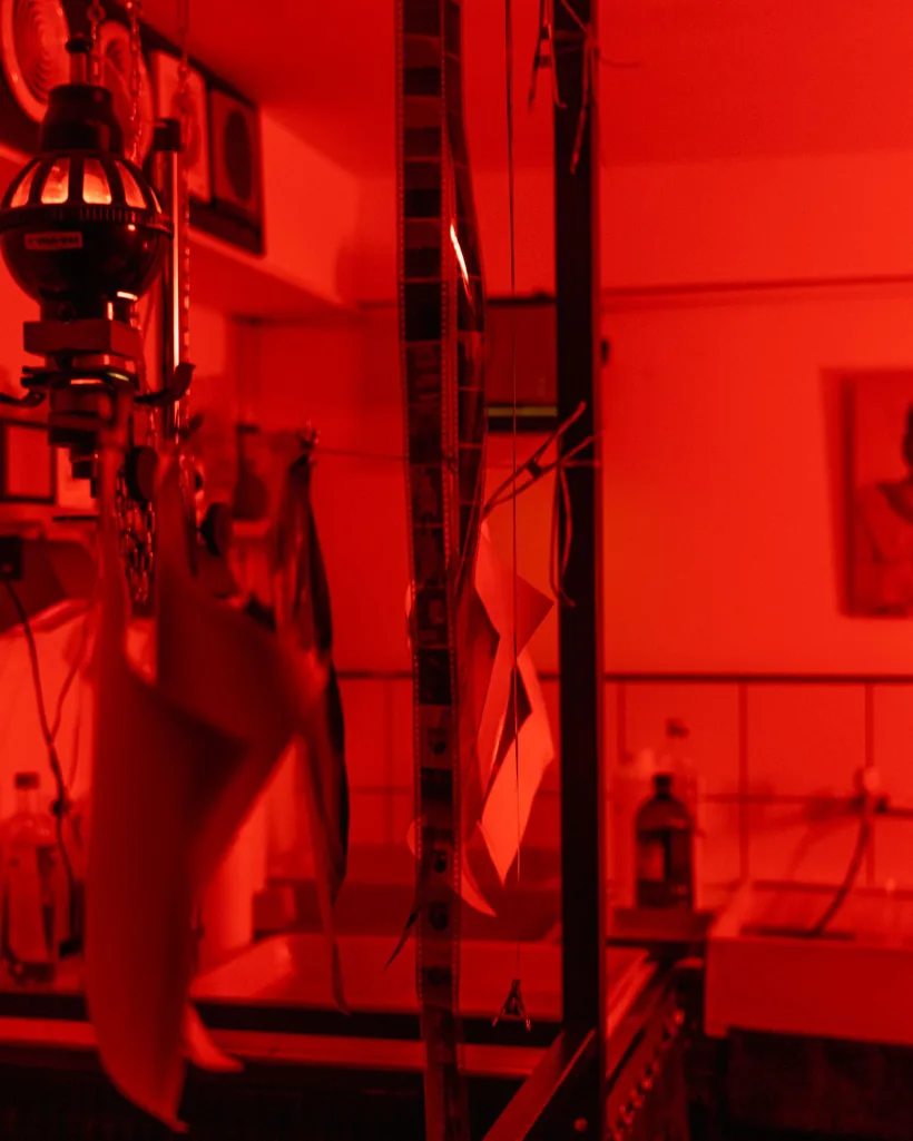 Tiras de negativos y copias colgadas con pinzas para secar en un laboratorio bajo luz roja